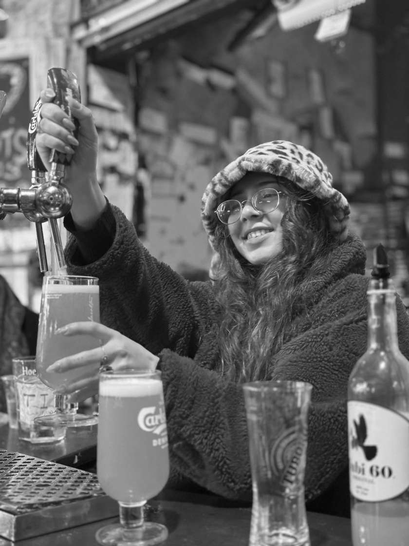 Carmel behind a bar in the Mahane Yehuda market pouring a beer
